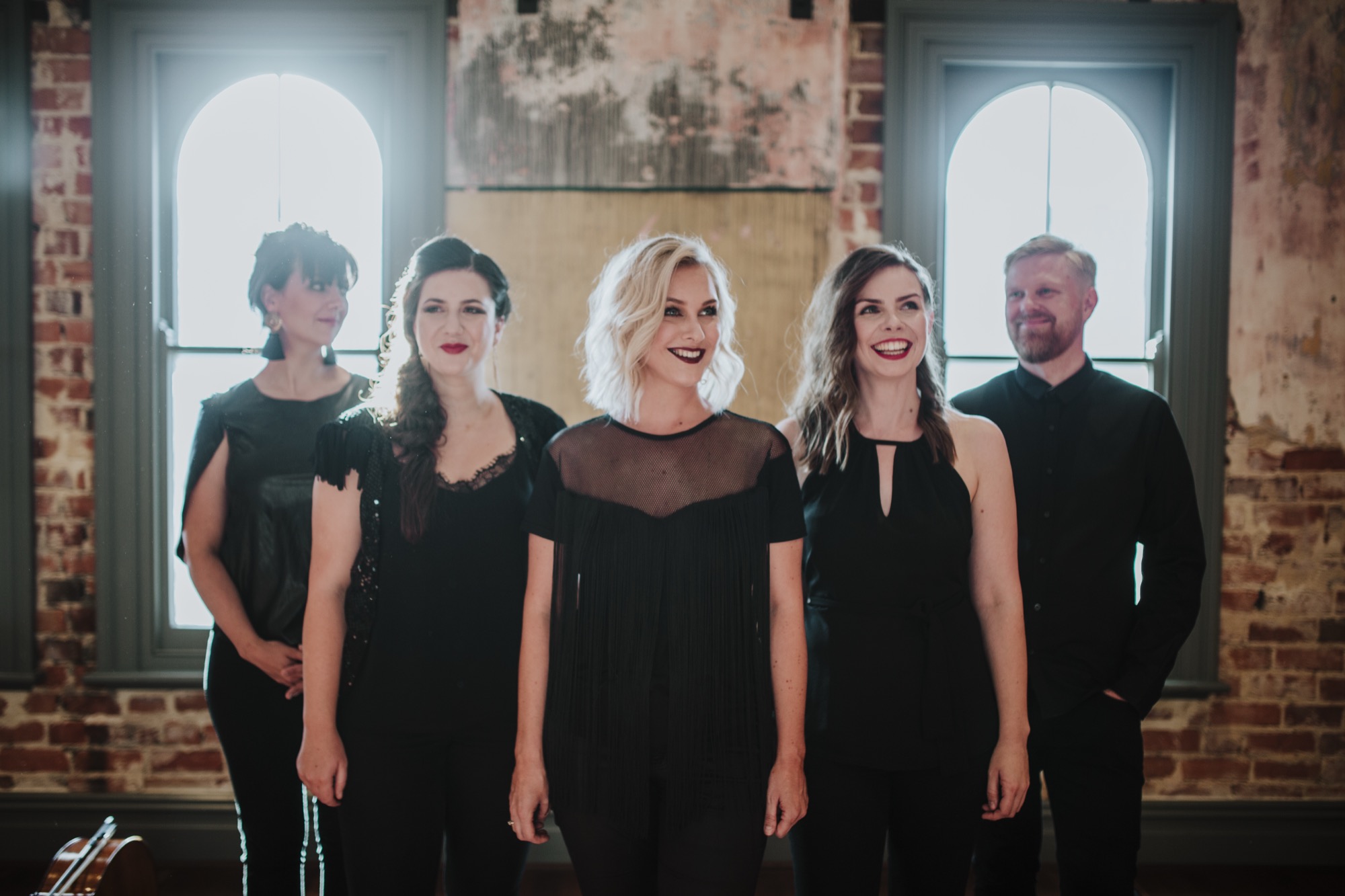 The Aquila ensemble in black, standing together in a light-filled brick venue