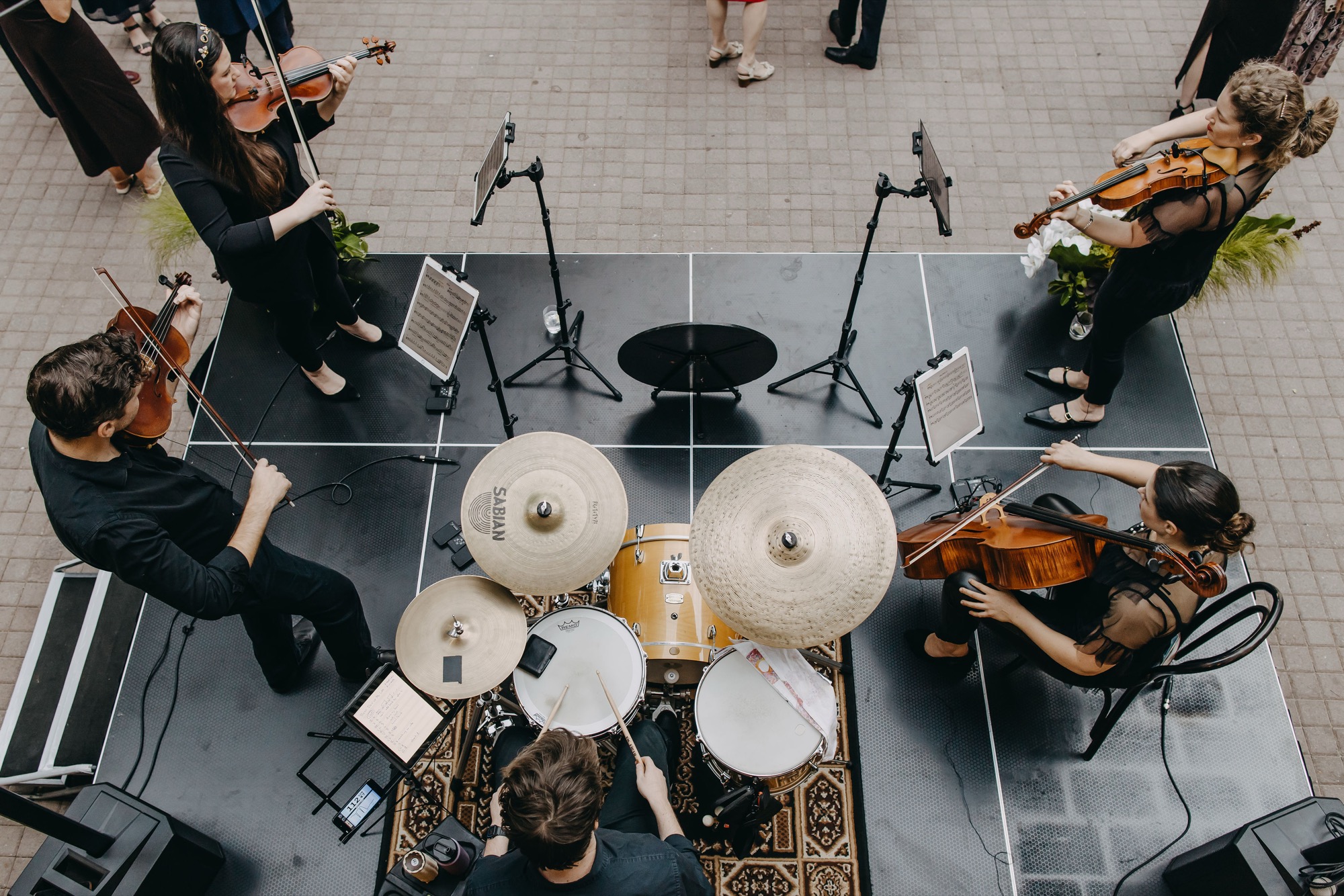 Overhead view of the Aquila ensemble performing live — strings and drums — at an event
